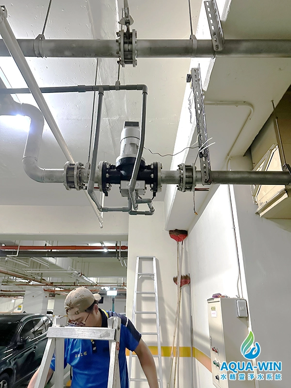 Close-up view of a vertical automatic backwash filter unit installed on a horizontal main water line with bypass piping in a commercial building's utility area.